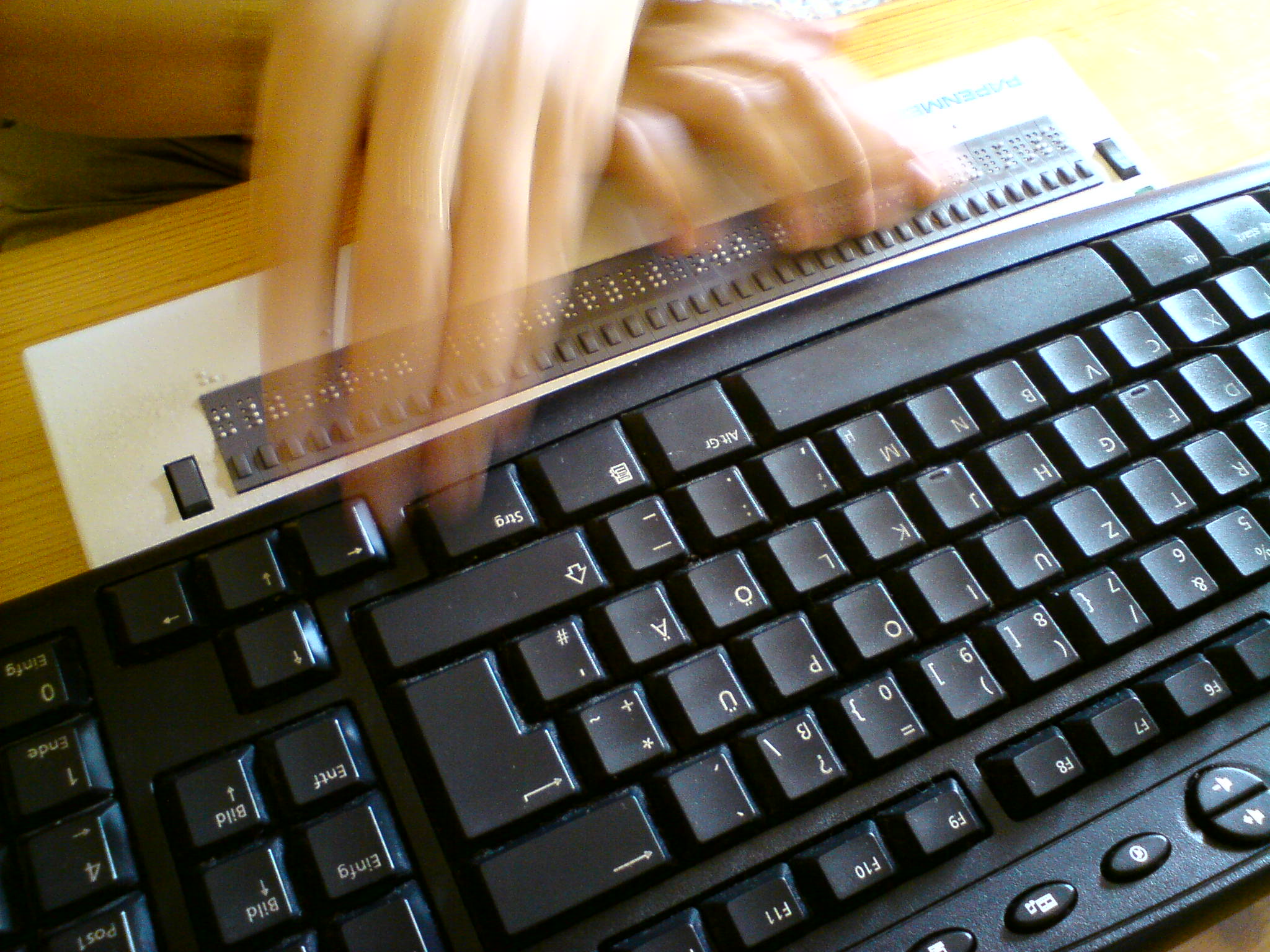 Foto: Hände in Bewegung über PC-Tastatur und Braillezeile